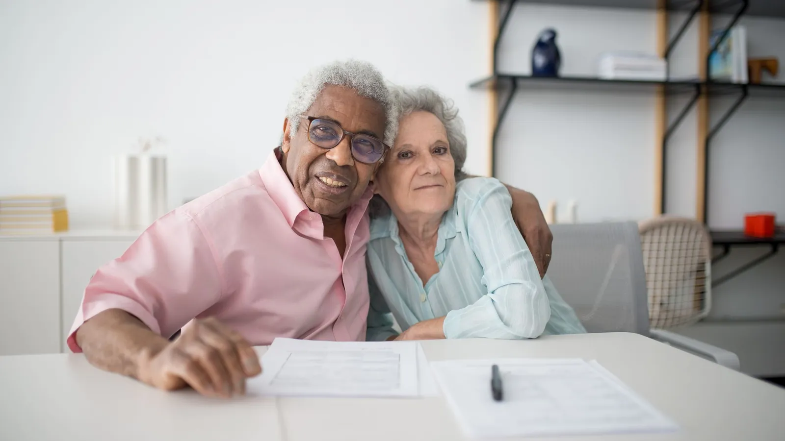 Un couple de seniors assis côte à côte à une table devant des formulaires et un stylo