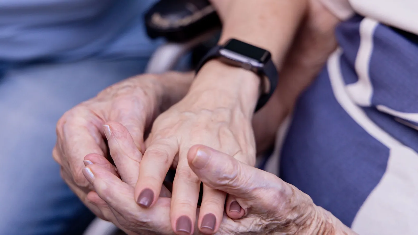 Gros plan sur les mains d’une personne âgée tenues par celles d’un proche
