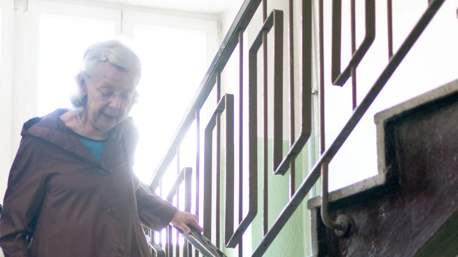 Une femme âgée descend un escalier en tenant la rampe