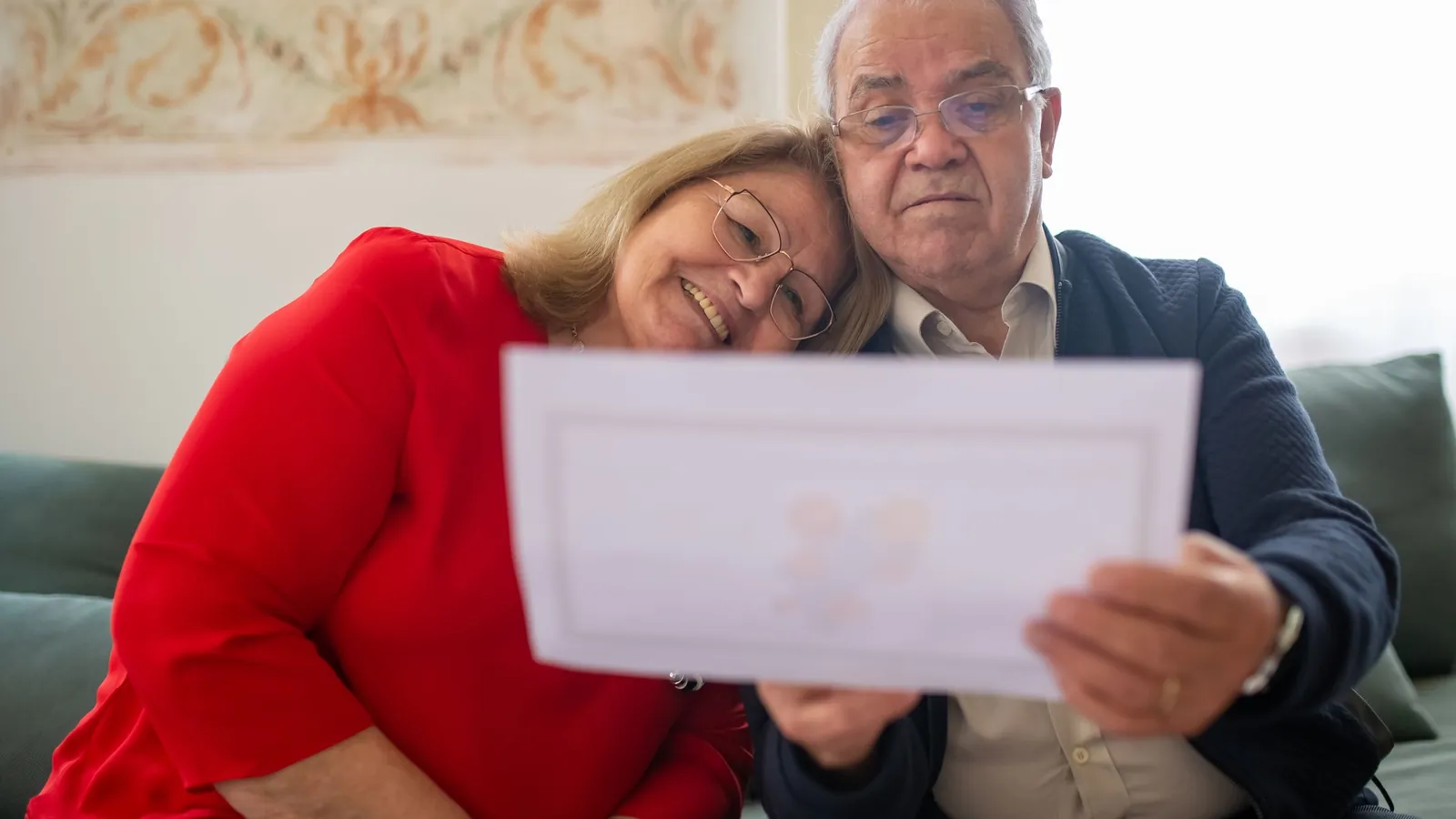 Un couple de personnes âgées assis sur un canapé regarde ensemble un document