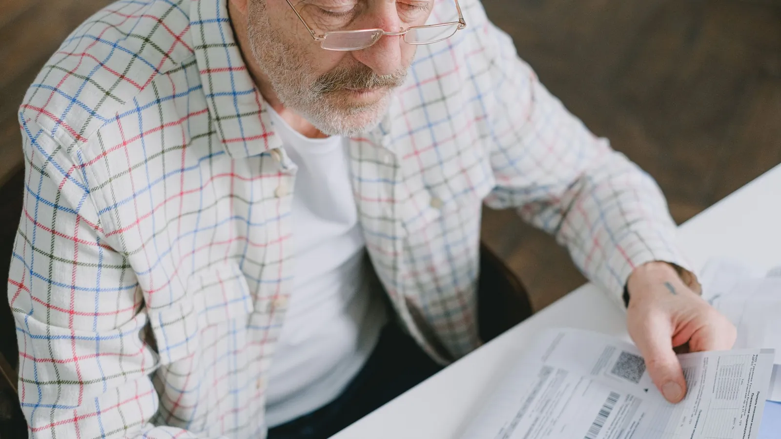 Un homme âgé à lunettes examine attentivement des documents posés sur une table