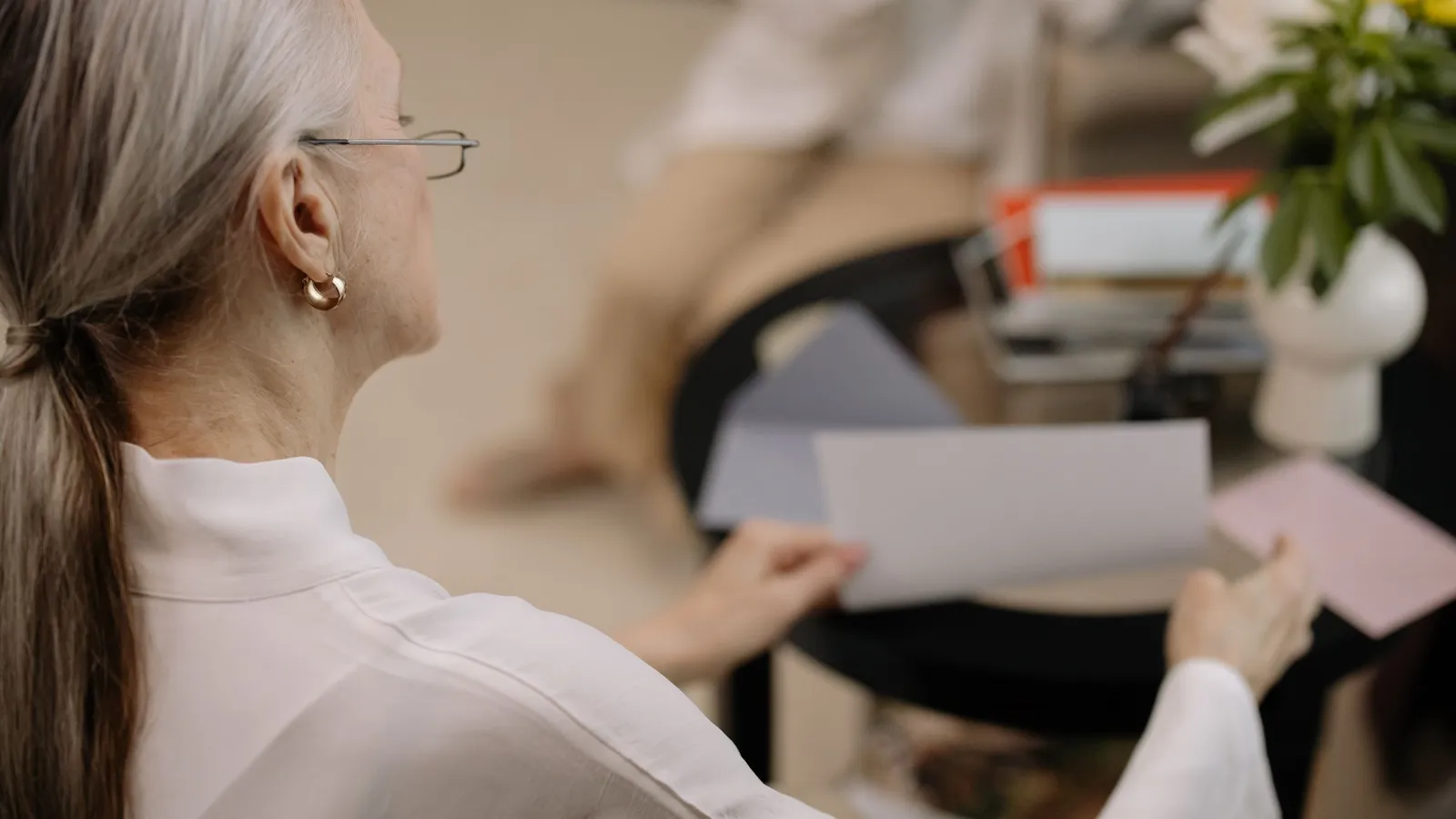 Une femme aux cheveux gris et à lunettes examine des papiers chez elle