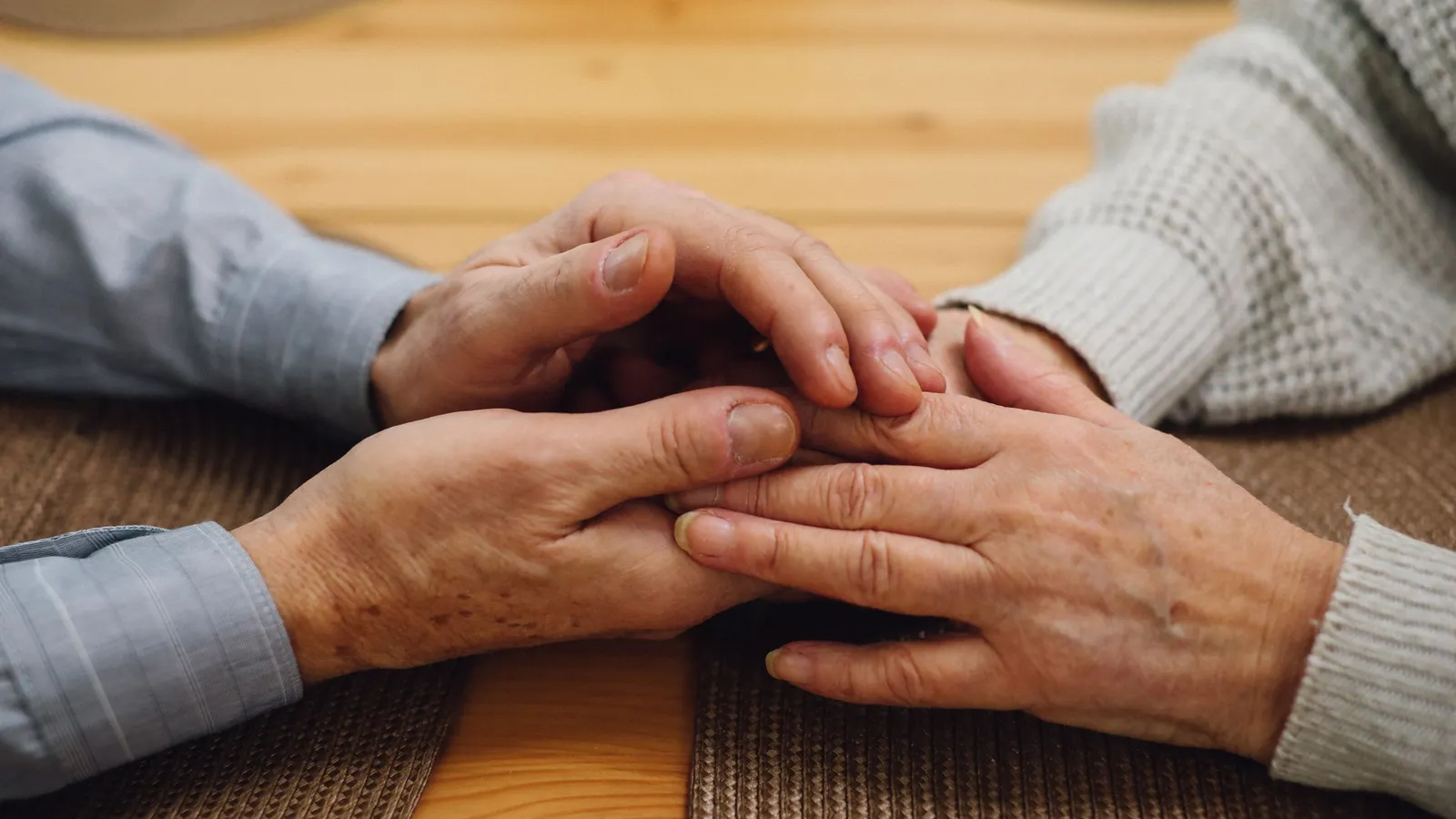 Deux couples de mains de personnes âgées posées l’une sur l’autre sur une table en bois